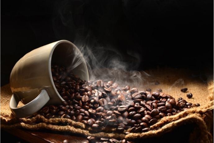 Xícara virada em pano marrom com grãos de café