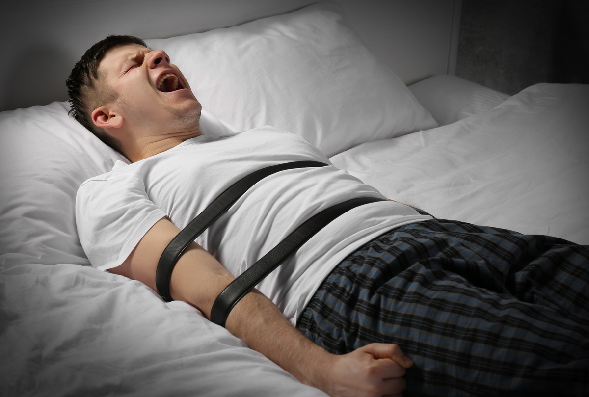 Homem amarrado em cama enquanto grita, uma das sensações mais recorrentes provocadas pela paralisia do sono.