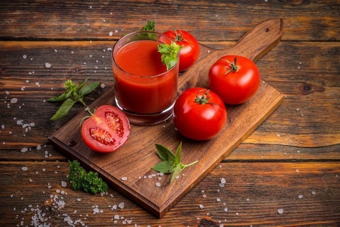 Tomates e copo com suco de tomate em tábua de madeira