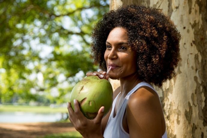 Mulher tomando água de coco em local arborizado 