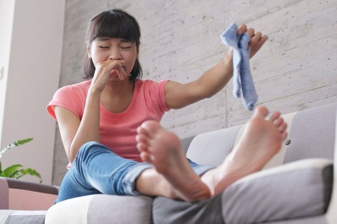 Mulher sentada no sofá segurando meias e tampando o nariz com as mãos