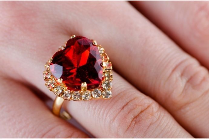Mão feminina com anel dourado com pedra de rubi