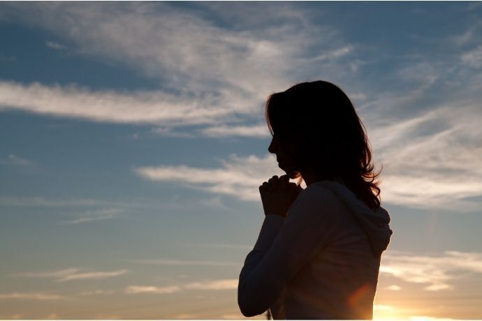 Silhueta de mulher em área externa rezando