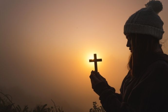 Silhueta de mulher segurando uma cruz no pôr do sol