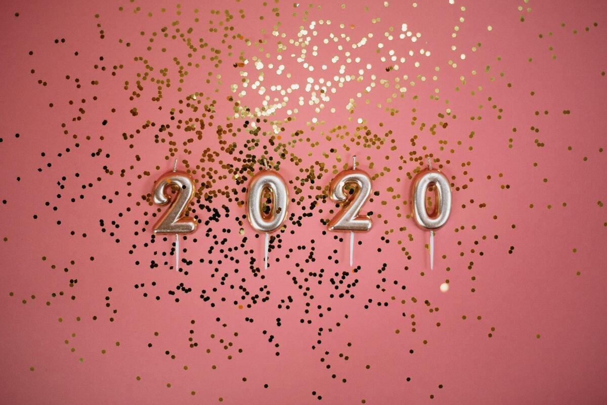 Velas com o número 2020 e confetes dourados ao redor em fundo rosa