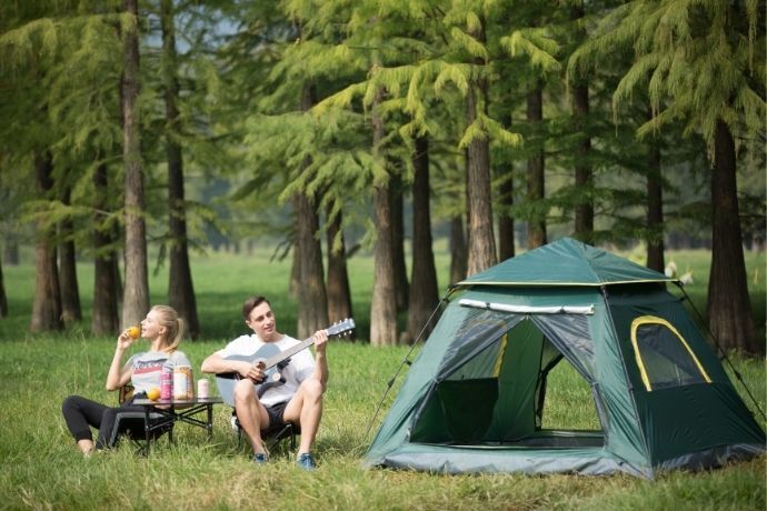 Casal ao lado de barraca de camping em clareira próxima a árvores