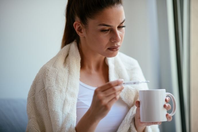 Mulher vendo temperatura em termômetro enquanto segura uma xícara de chá