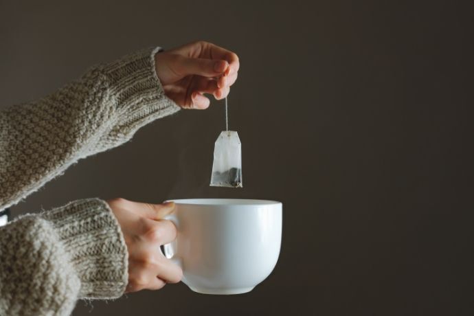 Mãos segurando xícara de chá e saquinho de chá