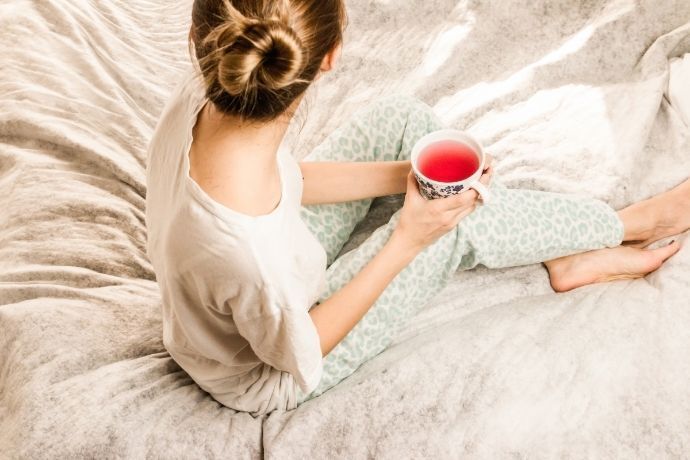 Mulher sentada na cama segurando xícara de chá vermelho