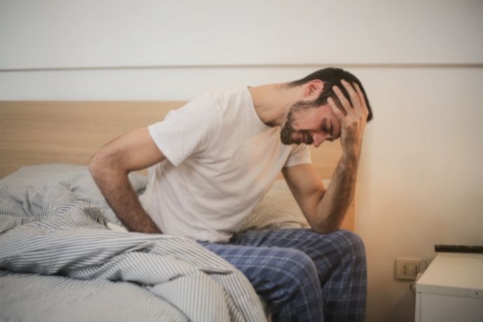 Homem sentado na cama sentindo dor de cabeça