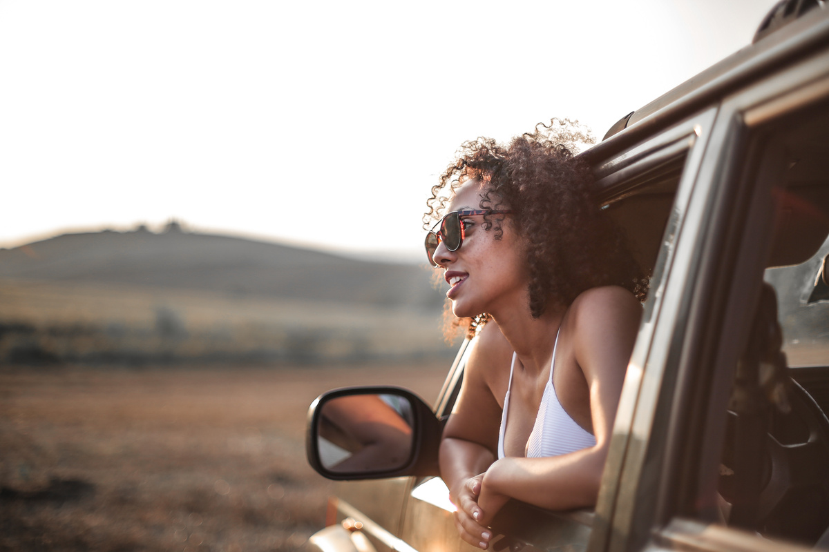 Mulher negra observando a paisagem de outro país pela janela de um carro preto.