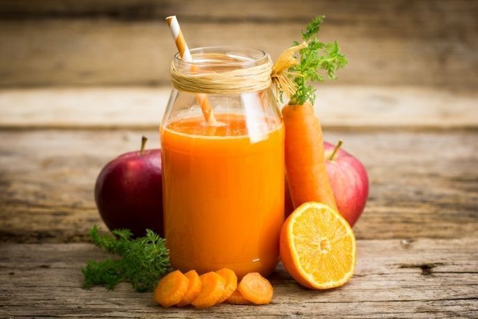Copo com suco de cenoura ao lado de maçã e laranja