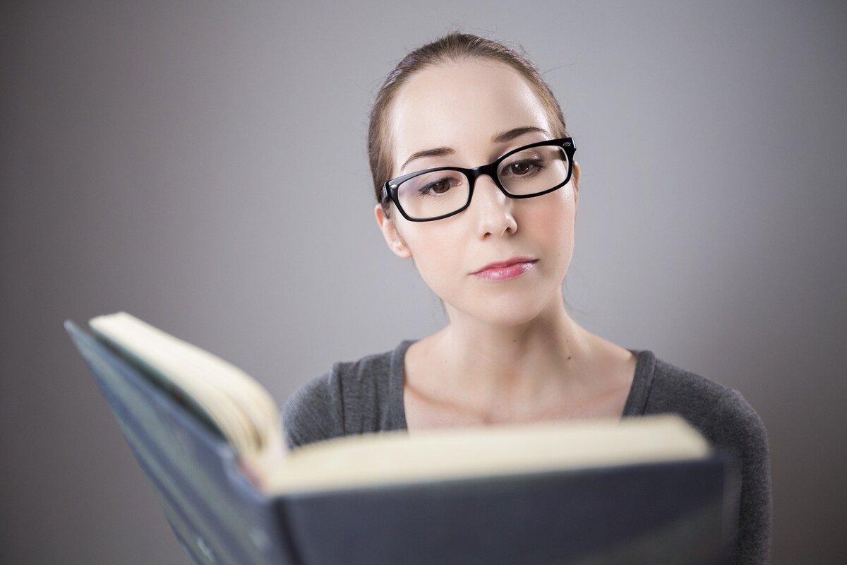 Mulher de óculos lendo um livro. 