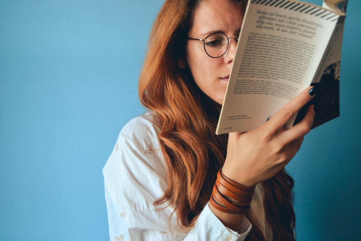 Mulher de óculos lendo um livro. 