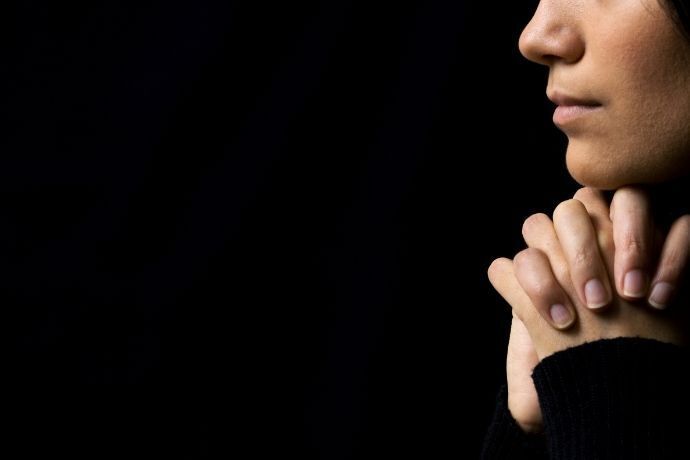 Mulher em fundo escuro fazendo oração