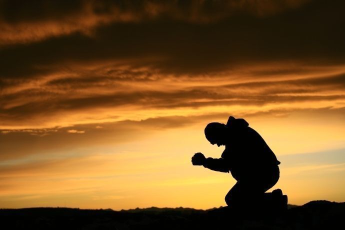 Homem ajoelhado no pôr do sol fazendo oração