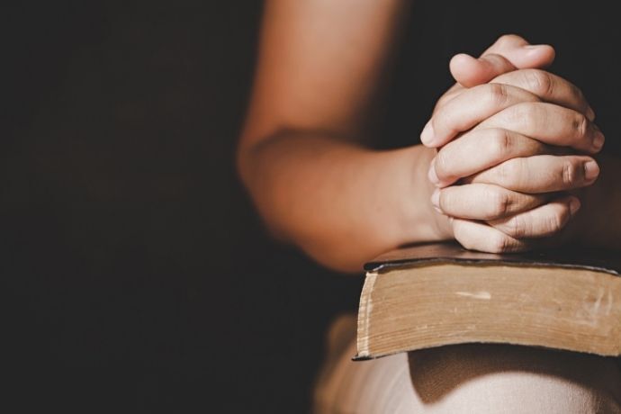 Mulher rezando com bíblia no colo