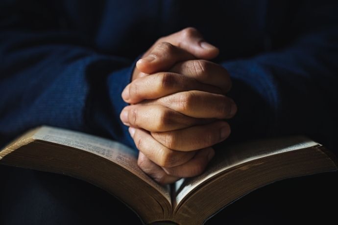 Pessoa com mãos sobre bíblia rezando