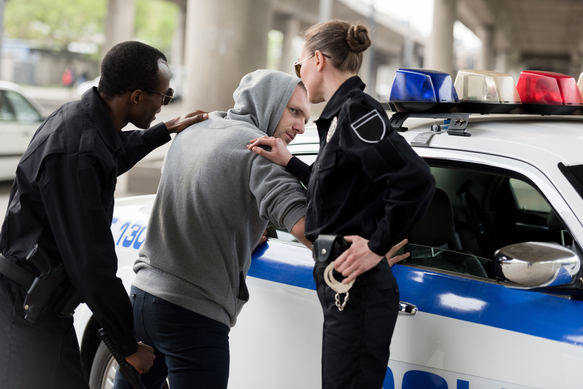 Homem sendo preso por dois policiais.