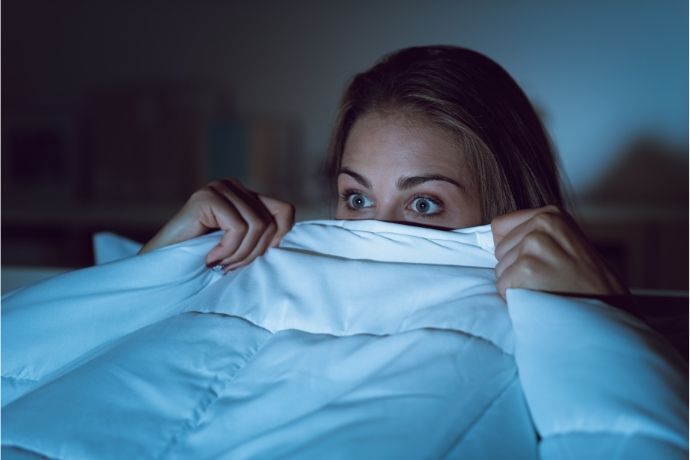 Mulher se escondendo em cobertor enquanto assiste filme de terror