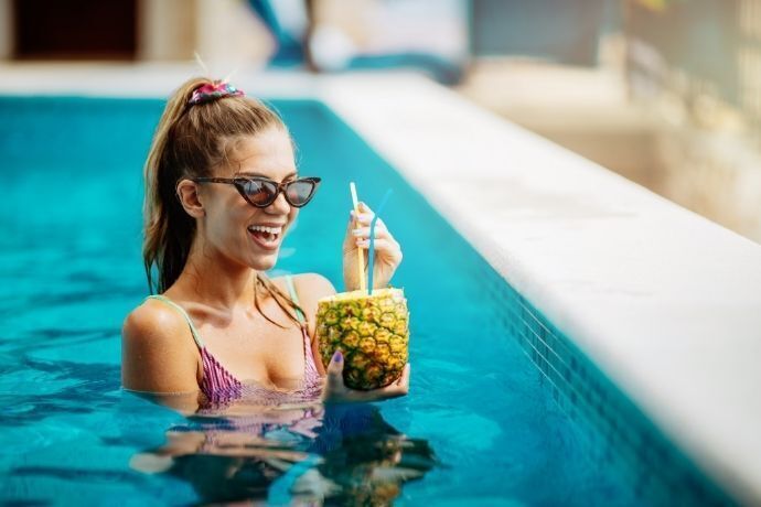 Mulher tomando drink em abacaxi em piscina de clube