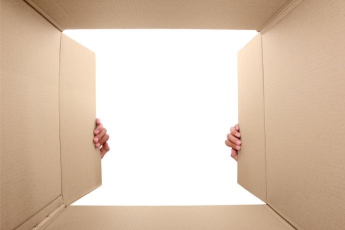 Vista de dentro de uma caixa de papelão com duas mãos abrindo a tampa