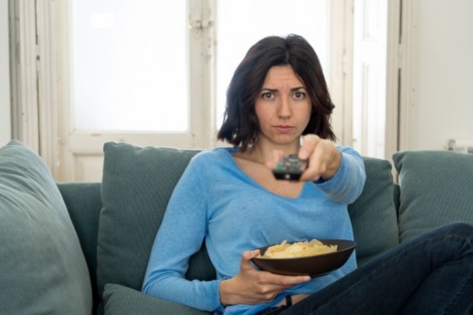 Mulher sentada no sofá segurando controle e prato de comida