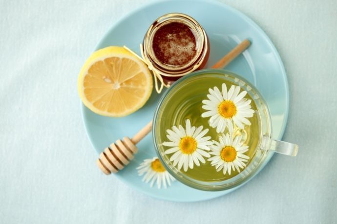 Xícara com chá de camomila, flores de camomila e limão partido ao meio
