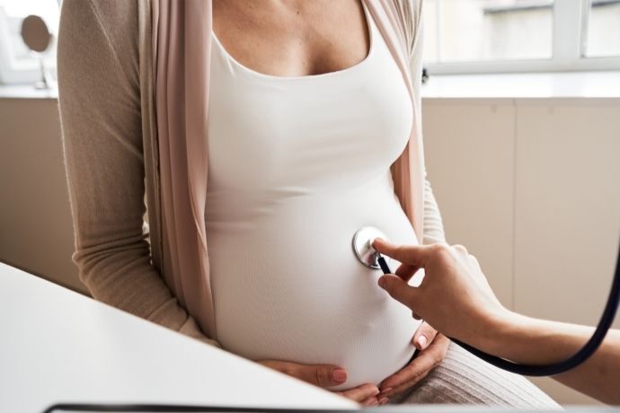 Mulher grávida em consulta com médico ouvindo batimentos na barriga