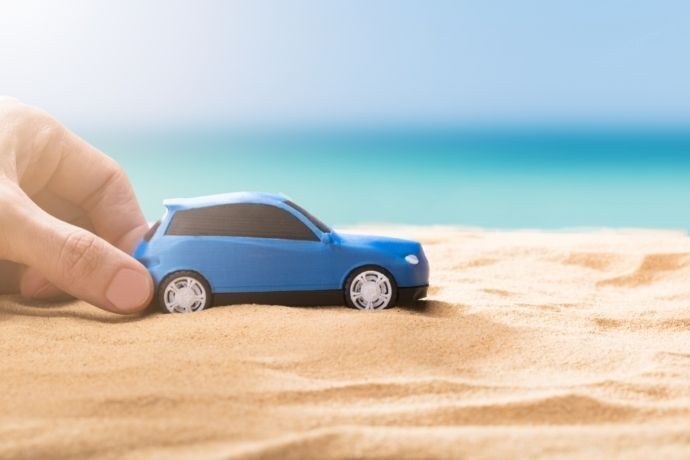 Mão segurando carrinho azul de brinquedo em areia de praia