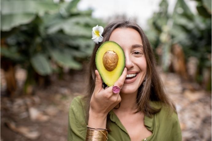 Mulher segurando metade de um abacate sobre o rosto