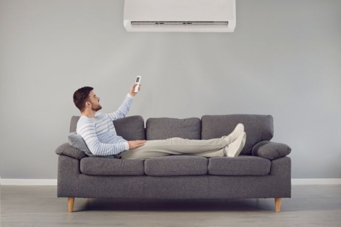 Homem deitado no sofá ligando ar condicionado com controle