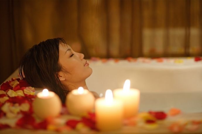Mulher tomando banho em banheira com pétalas vermelhas e rosas
