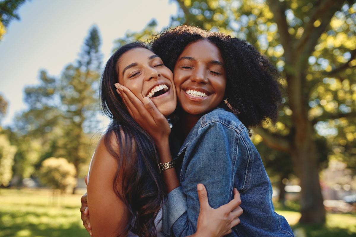 Duas mulheres sorrindo enquanto se abraçam forte, representando mulheres.
