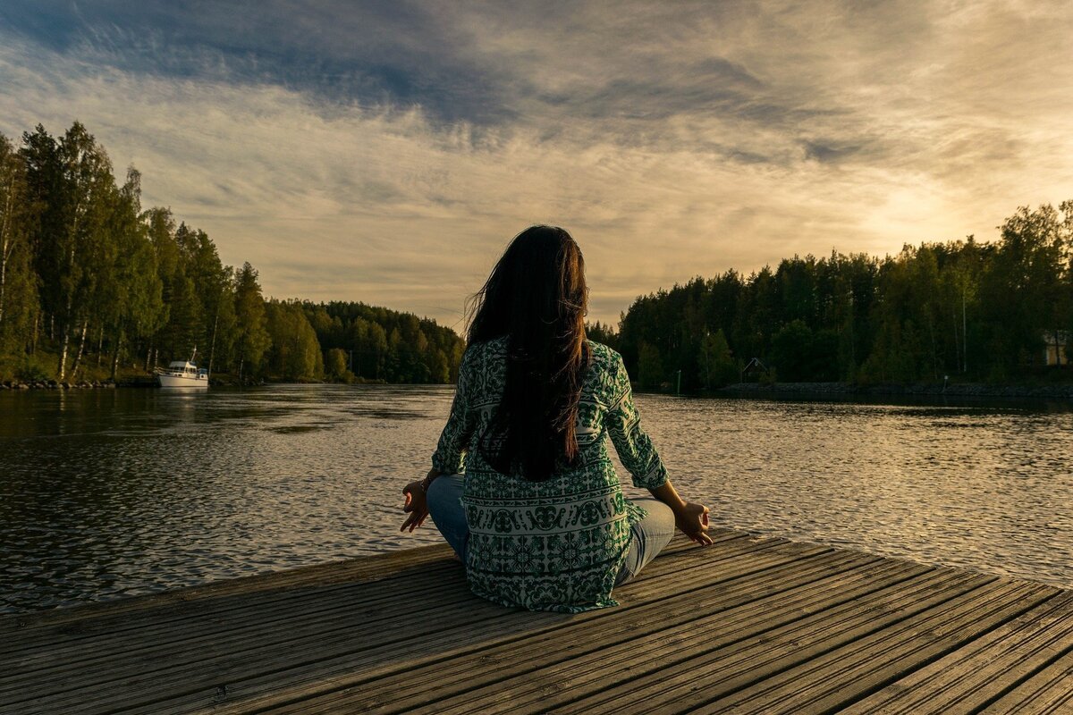 Mulher sentada em frente a lago enquanto medita e encontra calma, algo que é preciso ser feito para que a Lei da Atração funcione.