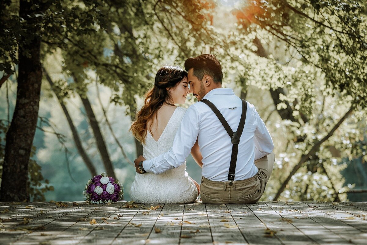Casal de homem e mulher, vestidos de noivos, sentados em meio à natureza, representando o amor conquistado pela Lei da Atração.