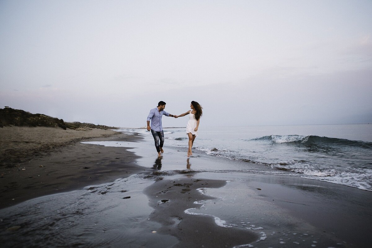 Casal feliz saltitando na beira da praia enquanto de mãos dadas, representando o efeito da Lei da Atração no amor.