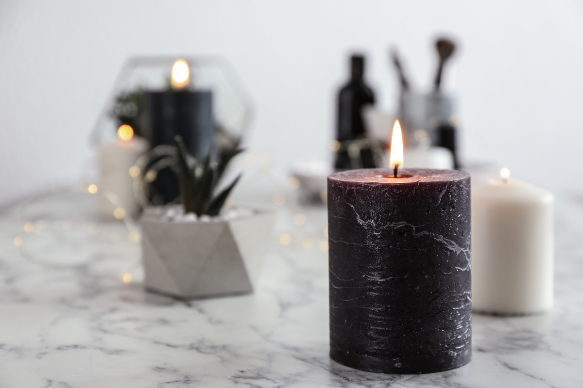 Vela preta acesa sobre mesa de mármore com velas brancas de fundo.