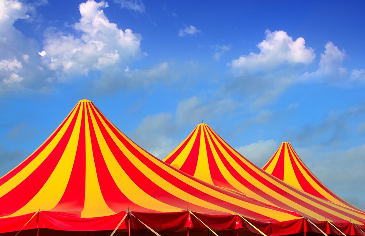 Imagem de lonas de circo de cor amarela e vermelha em meio a céu azulado.