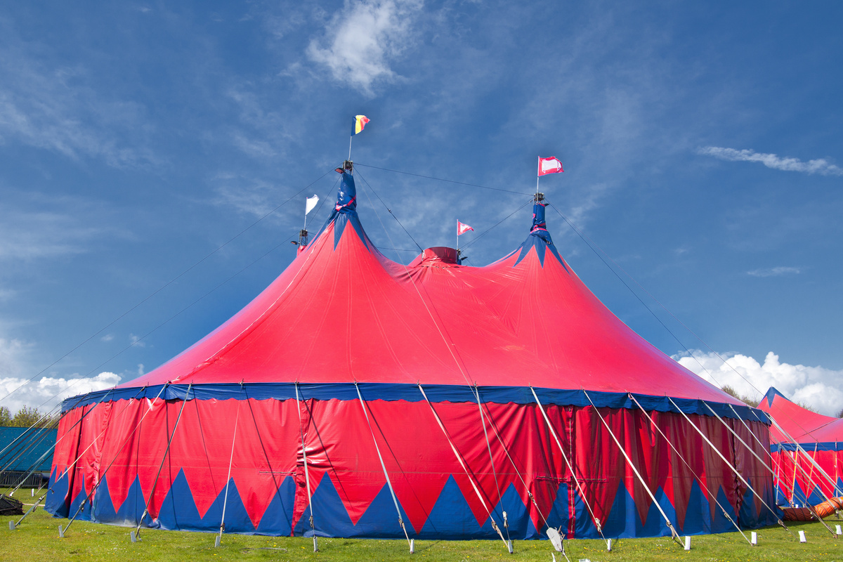 Grande estrutura vermelha de circo montada em gramado aberto.