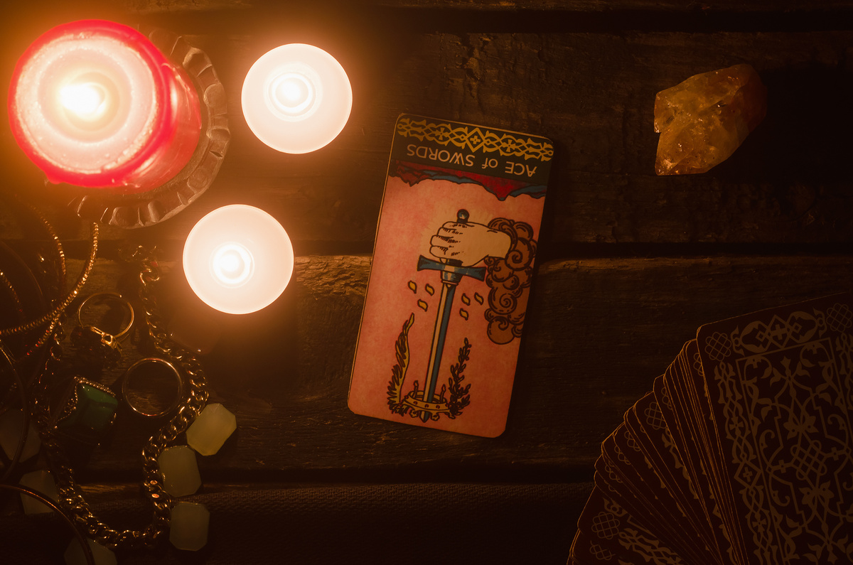 A carta Ás de Espadas iluminada por velas vermelhas em mesa de madeira.