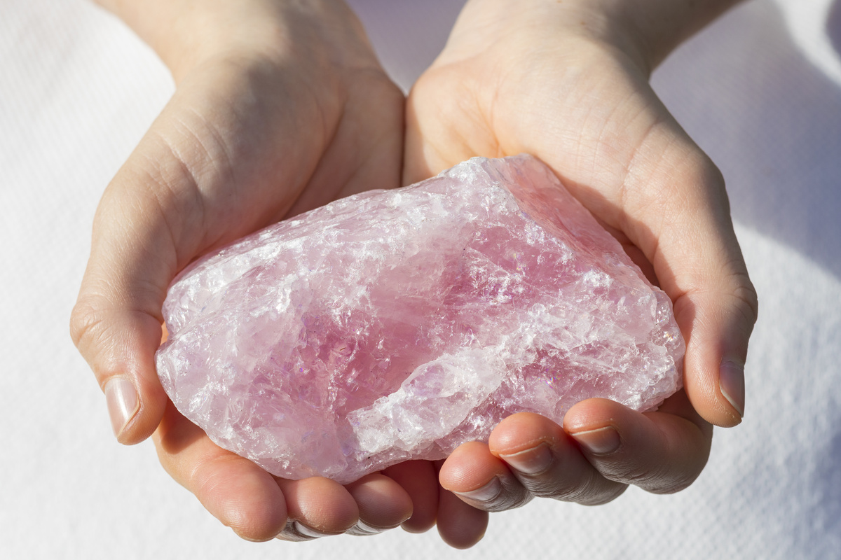 Pessoa segurando pedra bruta de quartzo rosa com as duas mãos.