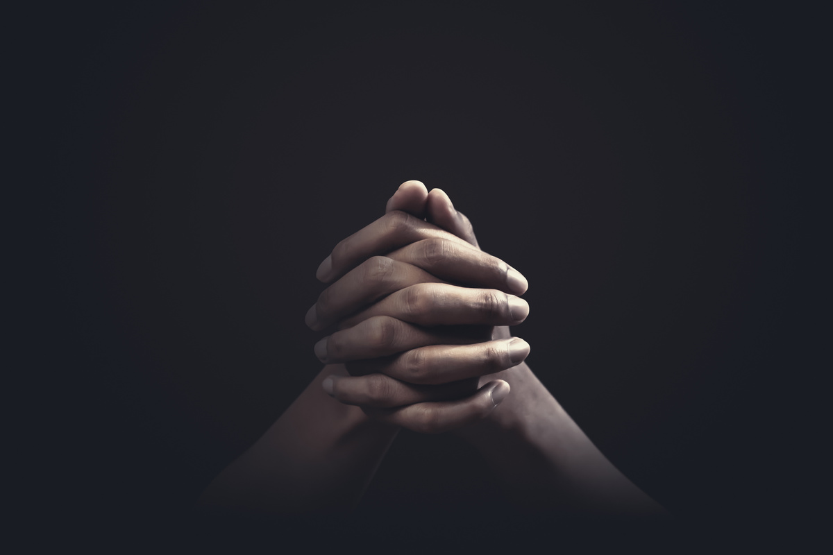 Mãos fazendo oração no escuro.