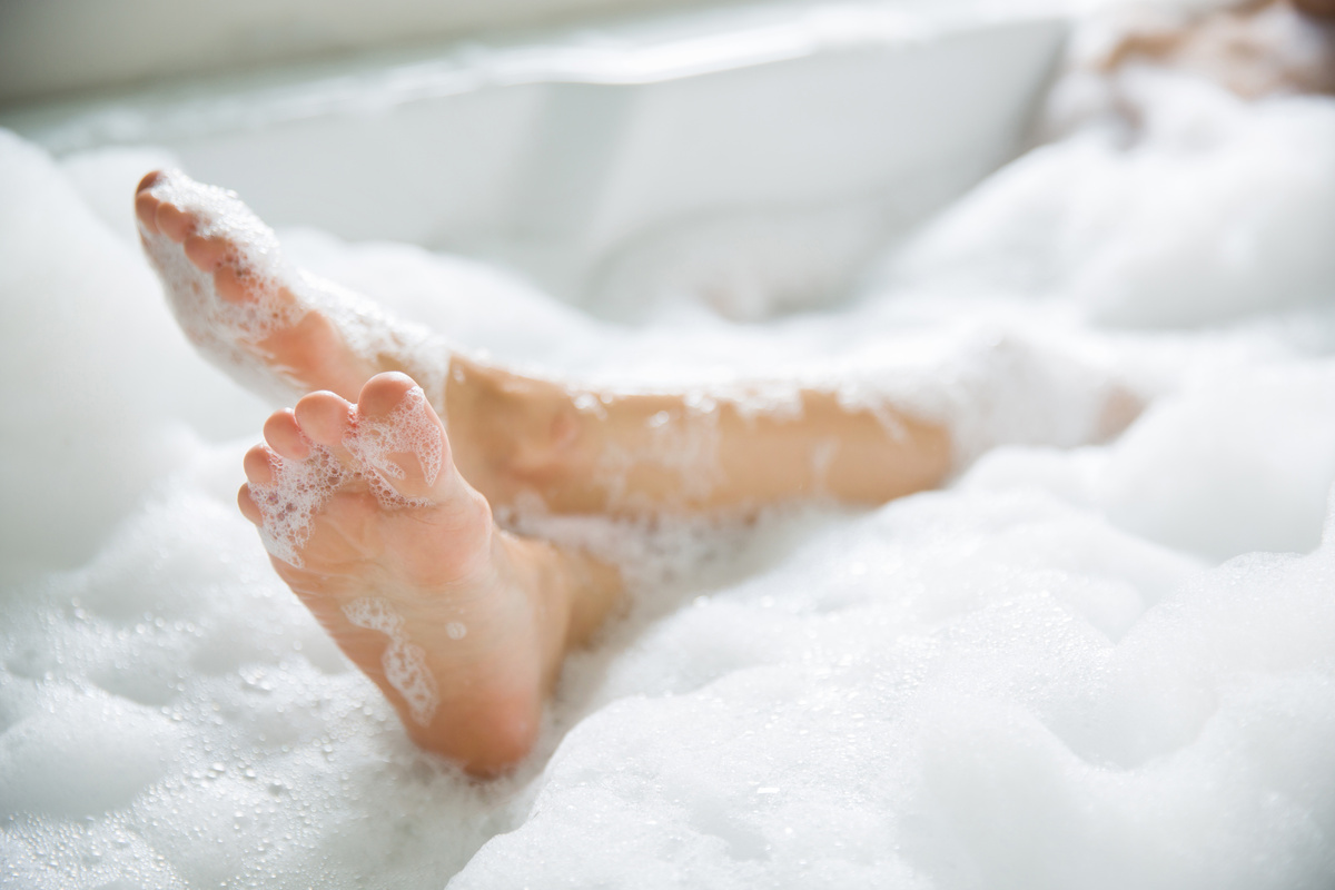 Pessoa com os pés cobertos de espuma e apoiados na beirada da banheira, simbolizando o banho para dar ânimo.