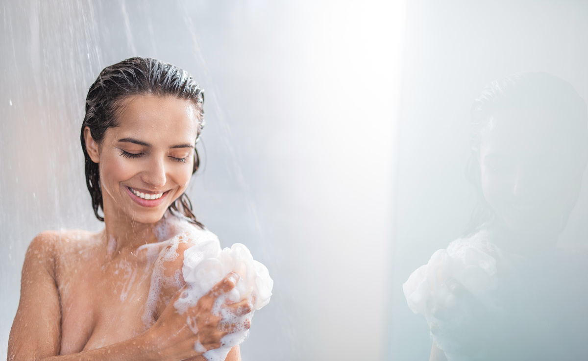 Mulher sorridente enquanto toma banho em ducha, simbolizando a prática do banho para dar ânimo.