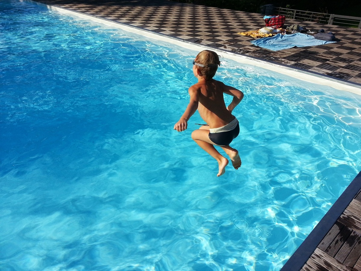 Criança pulando em piscina grande e de água limpa.