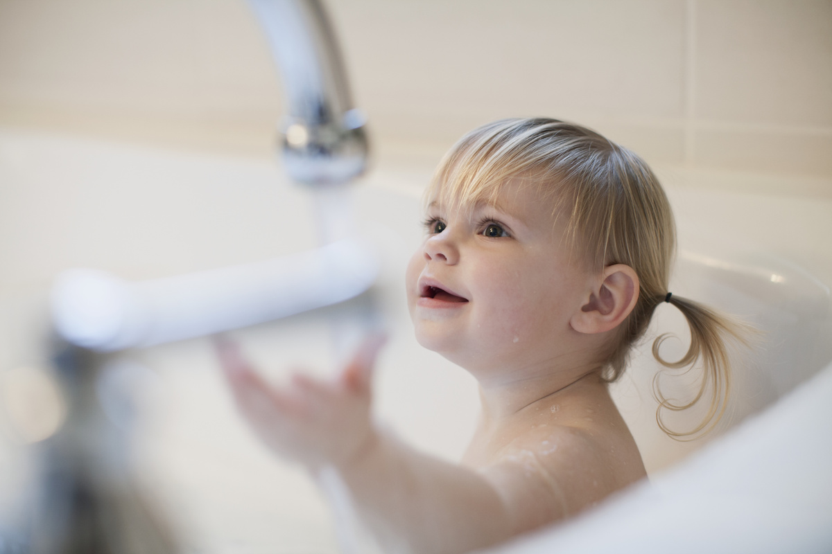 Criança loira sorrindo dentro de banheira.