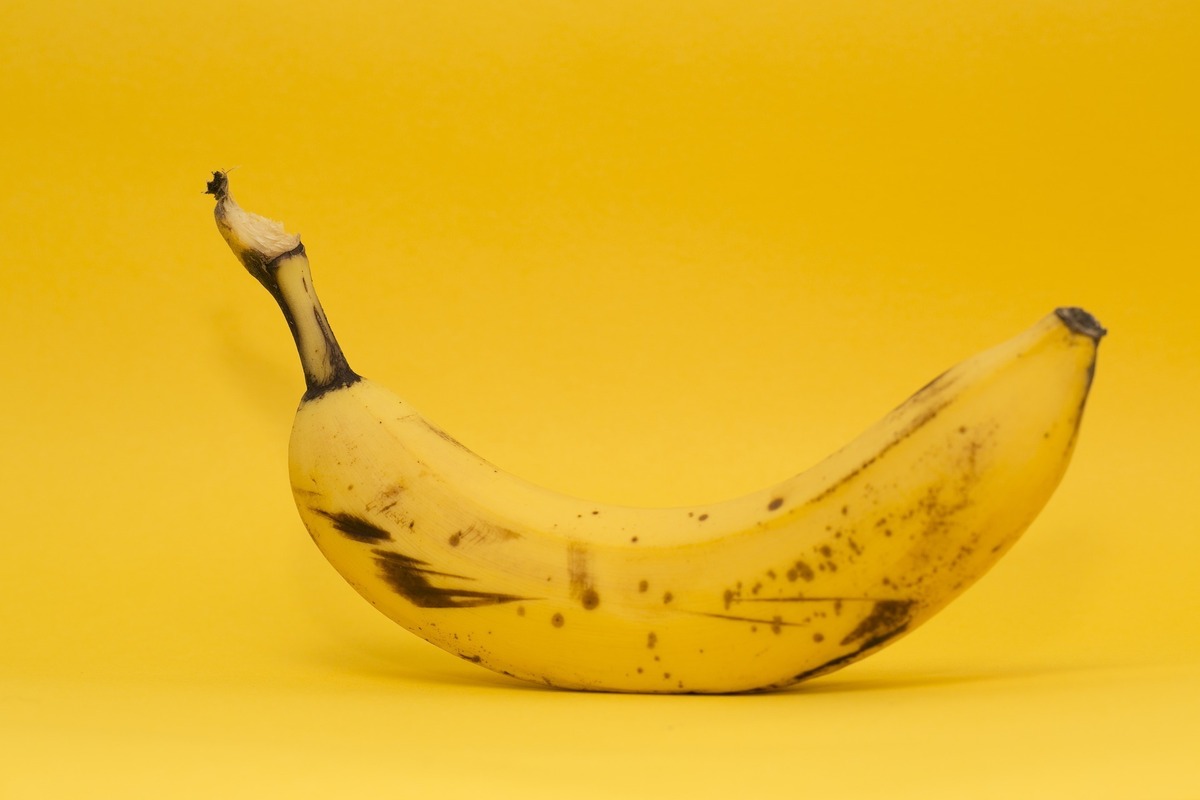 Uma banana madura em fundo amarelo, quase de mesma cor da fruta.