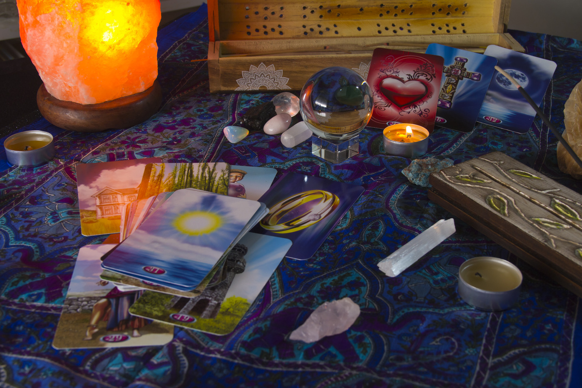 Cartas de baralho cigano em cima de mesa com toalha azul, algumas velas, cristais e uma bola der cristal.