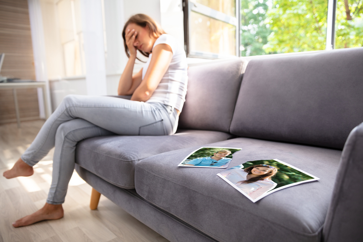 Mulher sentada no sofá triste com foto dela e do ex-namorado rasgado ao mei...